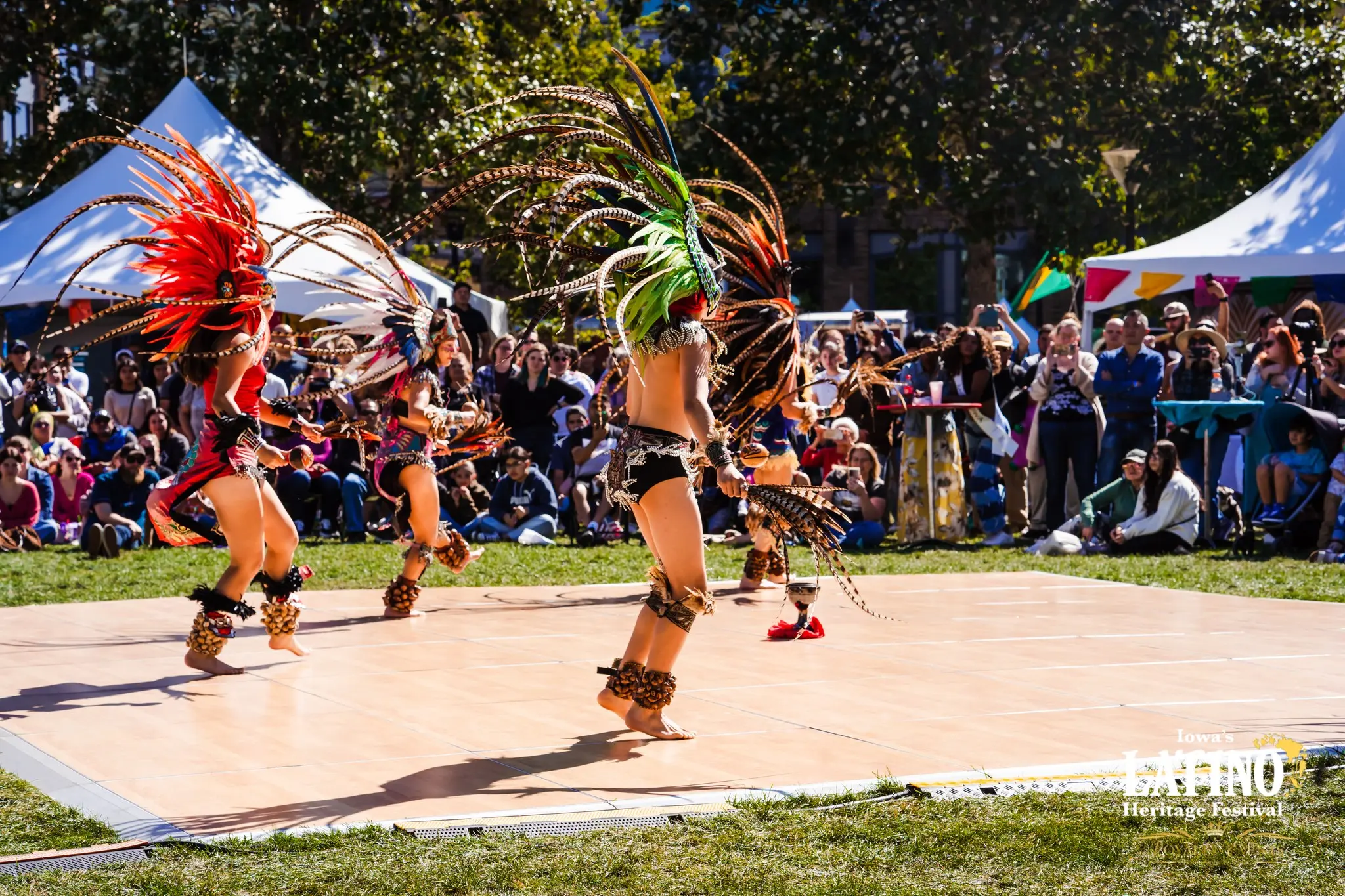 Four male dancers in traditional Latino clothes dance on a cement pad before a crowd.