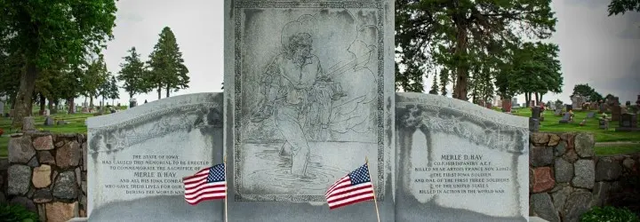 A large white stone memorial features a carved drawing of a man carrying a soldier's body.