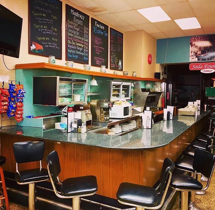 A green countered soda fountain featuring black stools and chalkboard menus.