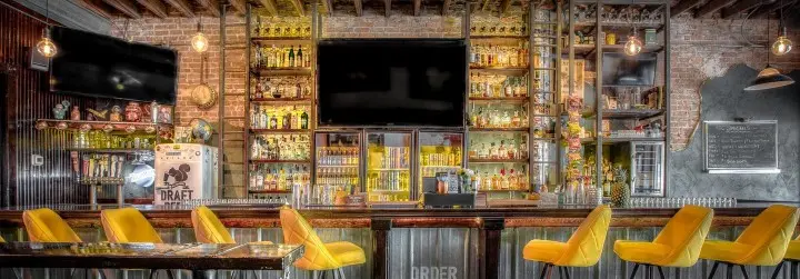 An extravagant tin bar with gold bar stools and a brick wall filled with liquors.