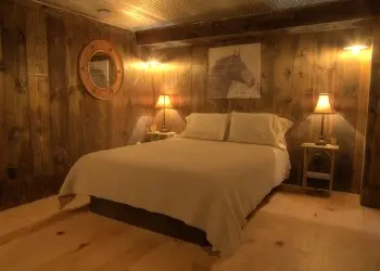 A wood paneled room with a white bed under a horse portrait and matching lamps.