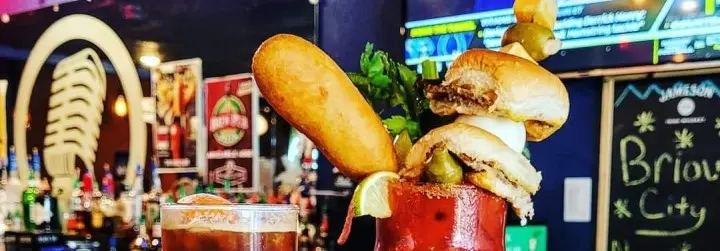 A Bloody Mary drink adorned with sliders, a corn dog and veggies. 