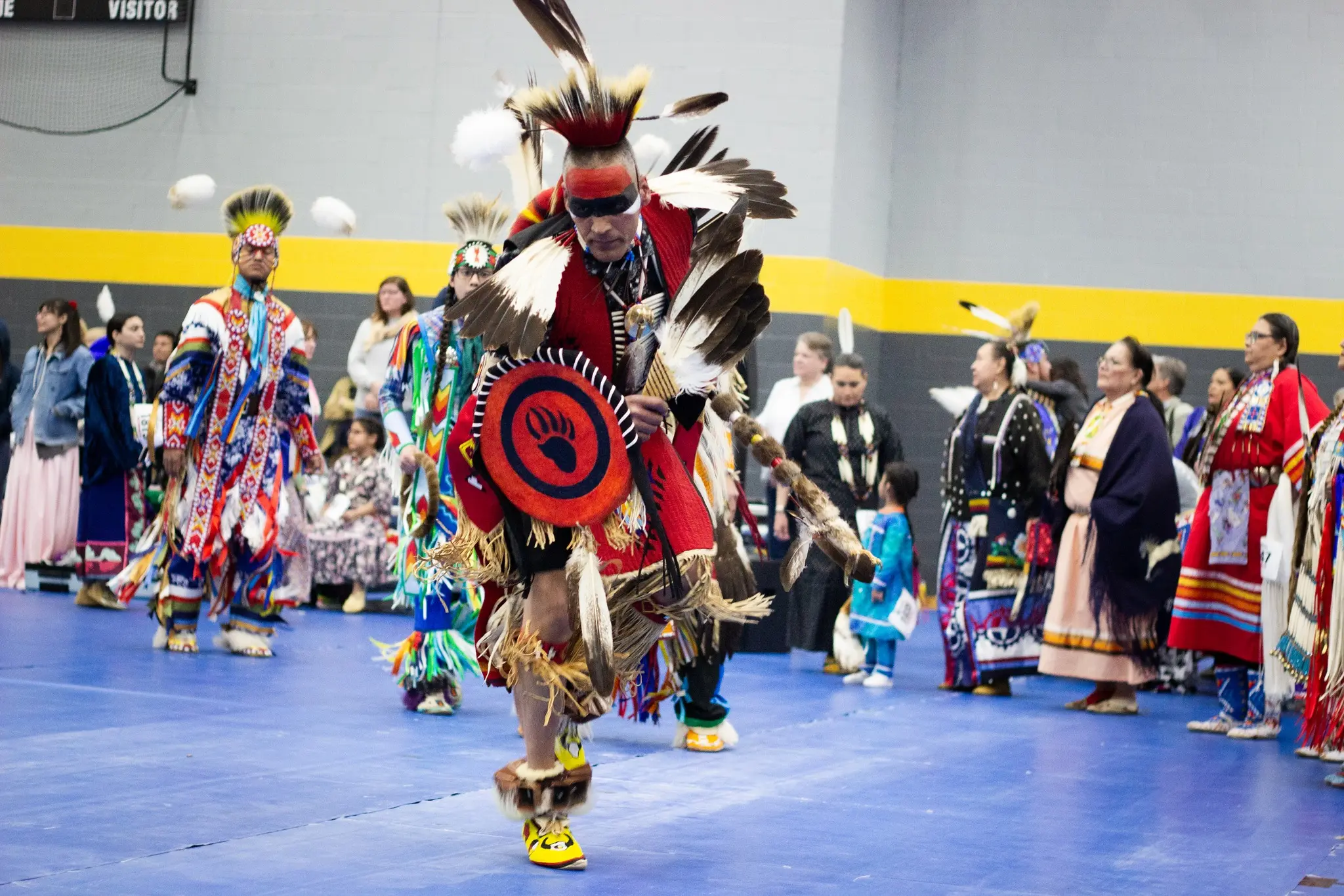 A Native American dressed in traditional clothing dances in front of a crowd.