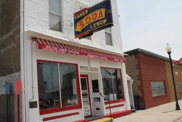 A historic white brick building with red trim surrounding the large front windows beneath a white and red striped awning.