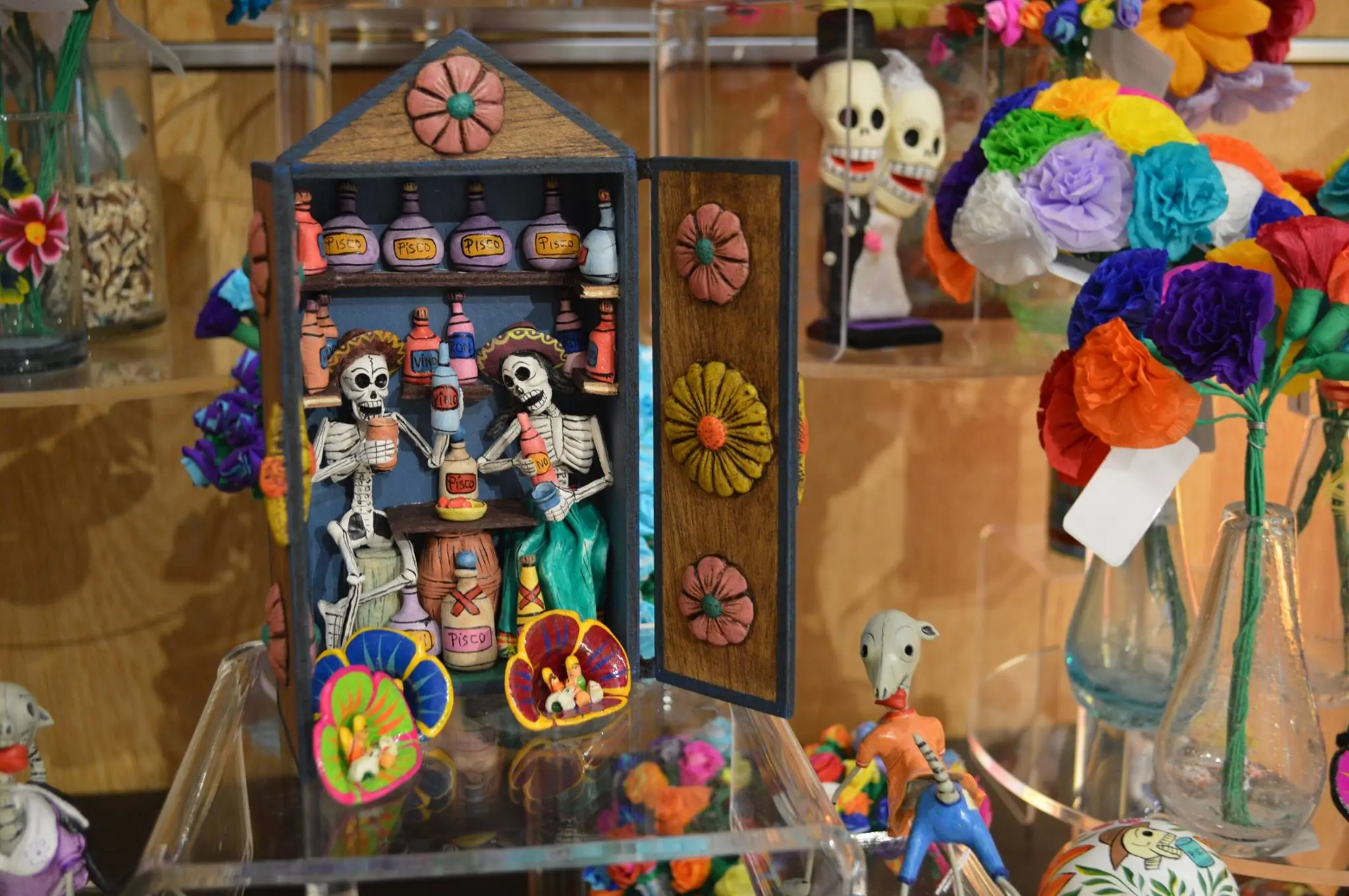Three decorative Dia de los Muertos skeletons wearing dresses sit inside a cupboard.