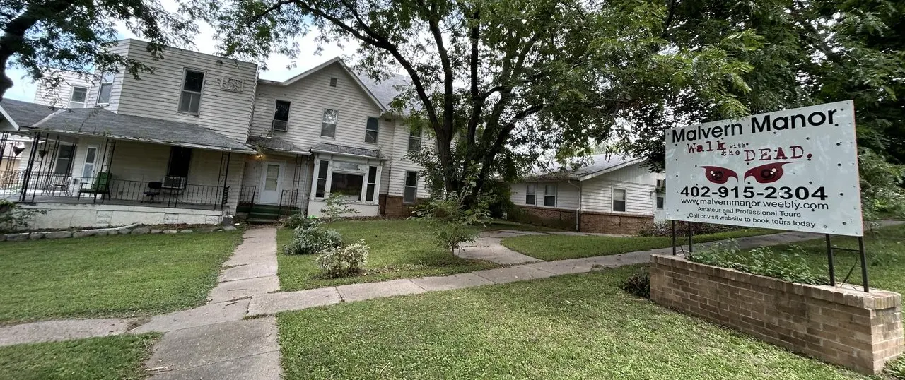 A seemingnly large abandoned home with a sign identifying it as the haunted Malvern Manor.